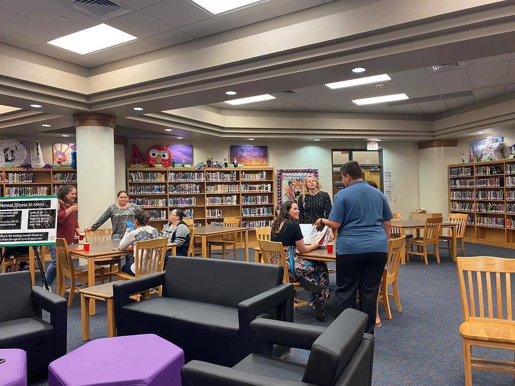 Group of teachers and students gathered around tables in the library. 